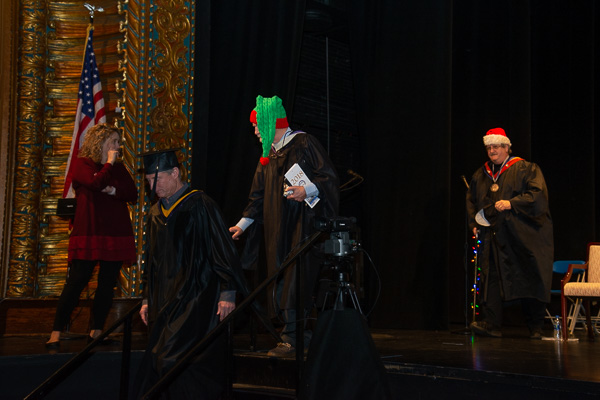 The final two faculty to leave the stage did so with seasonal flair: Tom Zimmerman (in green cap) and Chef Paul Mach (in Santa hat), his cane decked out with colored lights.