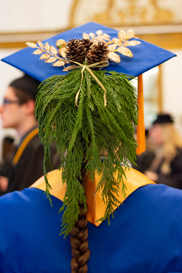 A horticulture grad adds pine to the pomp, seasonally dressing up her cap with mountain greenery.