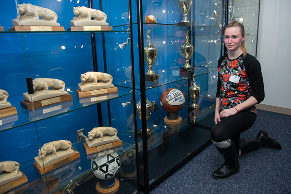 Obliging a photographer’s request, 2017 nursing grad Alicia N. Ross poses with the basketball touting her as the “Women’s All-Time Scoring Leader” with 1,515 points from 2014-17. The ball and other treasured trophies are displayed in the Athletics conference room. 