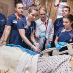 Nursing instructor Tushanna M. Habalar (in white), leads students in inserting an IV into “SimMan,” an electronically controlled patient simulator.