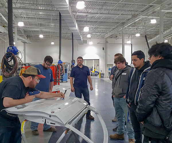 In a visit to the collision repair lab, students provide hands-on demonstrations to dual-enrolled high school students from Chester County. At center is Penn College instructor Loren R. Bruckhart.