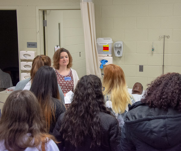 Val Myers, assistant dean of nursing, talks with students about what happens in ATHS W131, which includes simulation manikins and a student lounge area with computers, printers and couches.