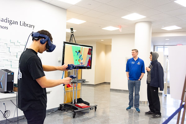 Esports team captain Jonathan W. Best (left) and head coach Joshua D. Young (in blue) promote the college's newest athletics addition with a virtual reality demonstration in Madigan Library.