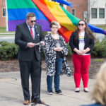 With the rainbow flag about to be raised, Elliott Strickland, vice president for student affairs, offers remarks. Also participating are Milden (center) and Sammie L. Davis, coordinator of diversity and cultural life.