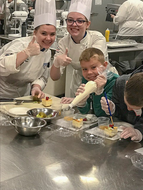 Baking and pastry arts students Autumn L. Schabener (left) of Reading, and Ashley L. Geist, of Huntingdon, help to lead children in creatively topping their cheesecake slices.
