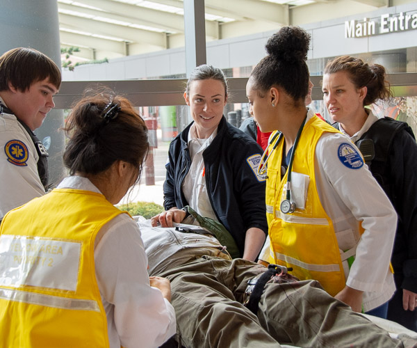Physician assistant students work alongside paramedics to assist physical therapist assistant student Brett W. Pehowic, of Lewisburg, who was very convincing in his role as a patient in severe pain. Included in photo are: PA student Reshma Sherpa, of Morrisville, N.C. (in yellow vest with back to camera), PA student Elizabeth A. Belz, of Montoursville, who participated in the drill in her other role as a Susquehanna Regional EMS paramedic (in blue jacket with white shoulder patch), and PA student Heidy C. Fernandez, of Bethlehem (in yellow vest and stethoscope).