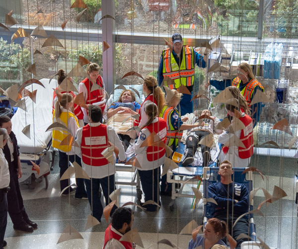 Students and health care professionals surround mock patients in the temporary emergency care area set up in the hospital lobby.