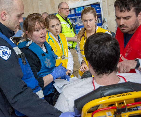 PA students – in yellow and red vests – gather information from a patient and the paramedics transporting him to the hospital. From left are Breica N. Beck, of Mountville (in yellow vest with blue stethoscope), Danielle N. Bilger, of Hollidaysburg (in yellow vest with purple stethoscope), and Timothy A. Bradley, of Williamsport (in red vest).