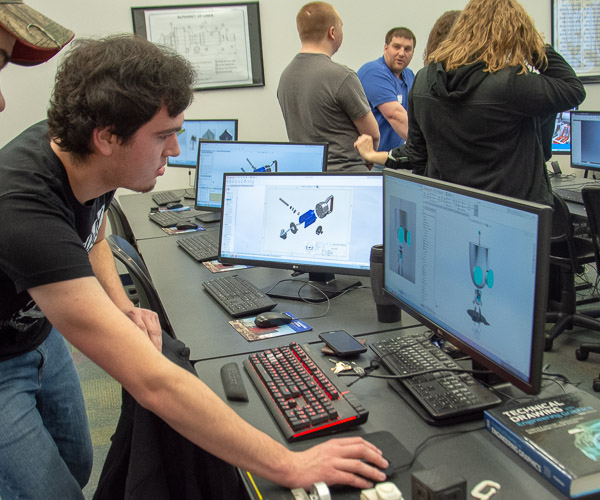 Cody A. Brown (foreground), an engineering CAD technology student from LeRaysville, and Jonathan F. DeRoner, ’15, computer aided product design (background), show projects to prospective students.