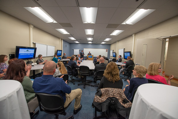Not your traditional “ribbon cutting”: President Gilmour (at podium) utilizes a tablet to turn on the lab’s monitors – to the applause of the audience. 