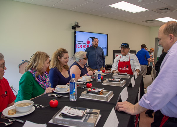 Ditchfield (in red apron) and his sous chef for the day, Food Bank board member Frank Pellegrino (on far right, in purple), present their appetizer to judges.