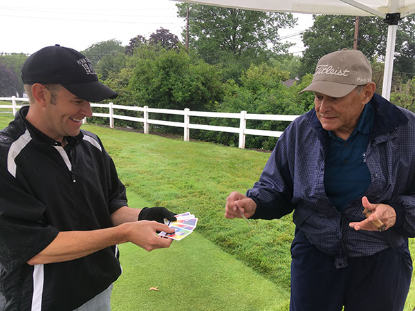 Pick a card, any card: Penn College golf coach Matt Haile (left) engages William Manos, of the sponsoring Fairfield Auto Group.