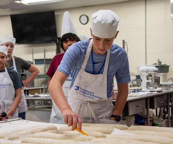 A participant slices the top of an Italian bread loaf to provide a means for steam to escape.