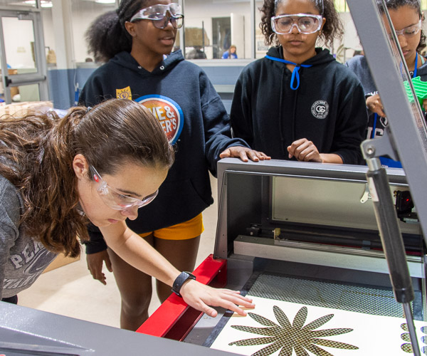 Mikayla (left), a repeat SMART Girls participant who decided to serve as a helper this year as the focus of her high school senior project, helps participants line up a project on the laser cutter.