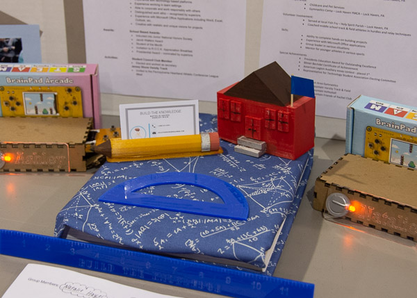 A team devised a cause called Build the Knowledge, which focuses on increasing education in the developing world. It would renew used textbooks with handmade book covers and donate them to schools that need them, and it would sell school supplies to fund the construction of schools. Included in the display are a book cover sample, a 3D-printed model school and 3D-printed business card holder, and business cards developed by the girls.