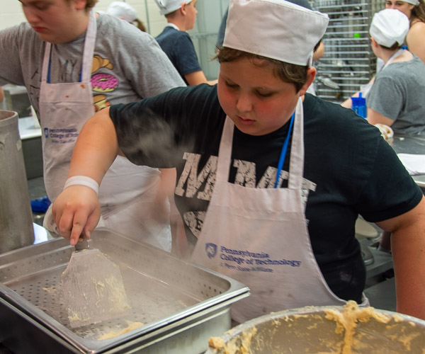 A young culinarian pushes dough through a perforated pan to form Spaetzle noodles.