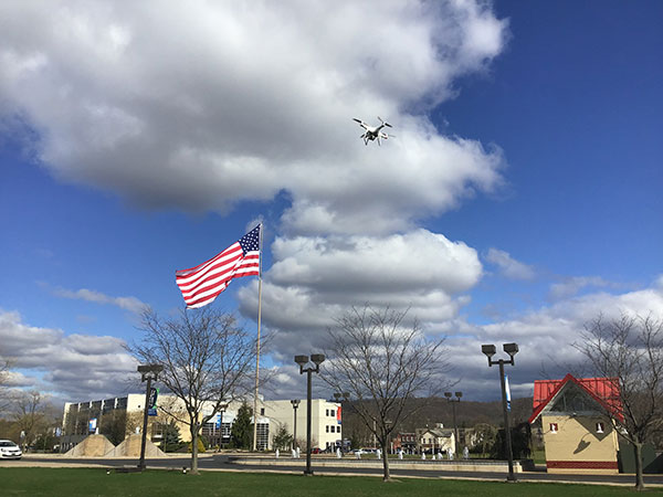 As the flag waves on a beautiful spring morning, a drone hovers in wait for instructions from its remote pilot.