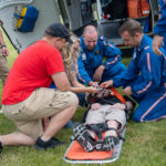 The Life Flight crew supervises as students strap a classmate onto a stretcher, detailing the protocol for loading a patient onto a helicopter.