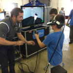 Collision repair instructor Shaun D. Hack helps a young fair attendee test his painting skills with the college's virtual reality spray simulator.