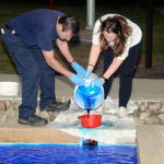 General Services' Gary T. Pandolfi, refrigeration, heating and plumbing mechanic, helps Katherine A. Downes, a graphic design major from Hamburg, as students took turns pouring Wildcat Blue dye into the water outside the ATHS. 