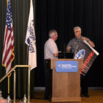 Brett A. Reasner (left), dean of transportation and natural resources technologies, accepts a Ford Performance banner for campus display after introducing Clor.