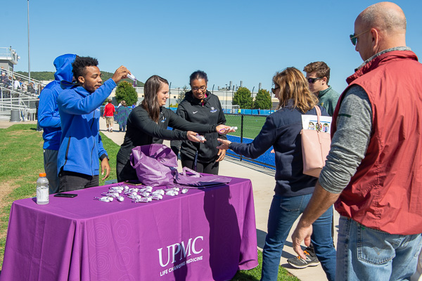 Student-athletes distribute UPMC bags and anti-bacterial gel to fans entering the complex. 