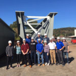 A class of afternoon visitors stands in the shadow of the plant's towering output.