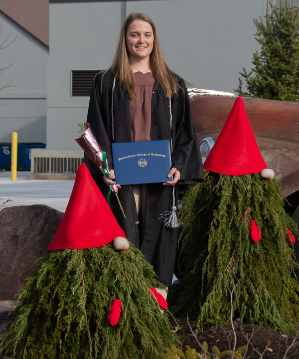 Erin M. Beaver, a welding and fabrication engineering technology graduate from Winfield, poses with evergreen gnomes. The award-winning metal sculptor is a fan of these clever creations of the college’s horticulture crew.