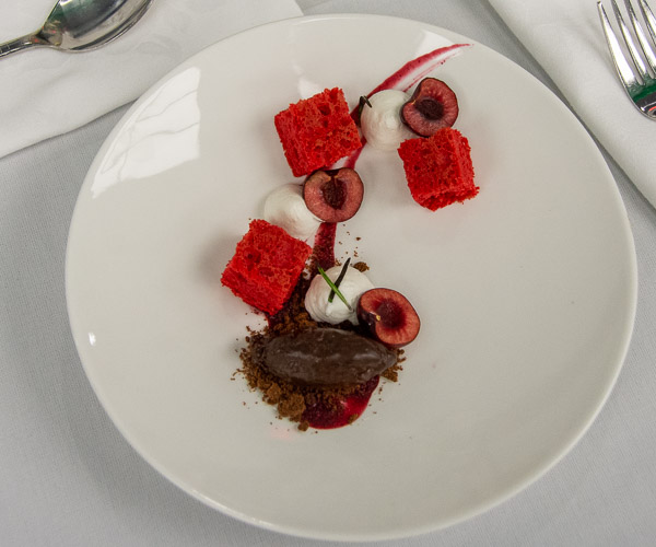 An “Inverted Black Forest” dessert: cherry sponge cake, Bing cherry halves, whipped cream, chocolate cremeux, crumbled chocolate tart, cherry coulis and rosemary sprigs.