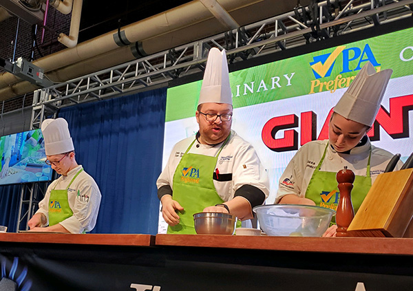 Grove (center), joined by Christopher M. Bashaw and Scatamacchia, shows the audience how to make Spring Vegetable Mac and Cheese. Bashaw is a culinary arts and systems student from Jersey Shore.