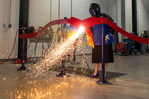 Pennsylvania College of Technology President Davie Jane Gilmour deftly wields a plasma cutter to sever a metal ribbon during a dedication ceremony for a greatly expanded welding facility at the college.