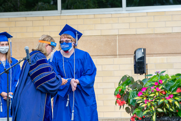 Face coverings and hand sanitizer were among the requisites to make in-person commencement a safe and socially responsible reality. Carolyn R. Strickland (left) vice president for enrollment management and associate provost, double-checks a student's name before the grad traverses the stage.