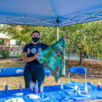Showing off the results of her tie-dye talents, Deanna M. Helverson, software development and information management, stays cool under a Wildcat blue canopy.