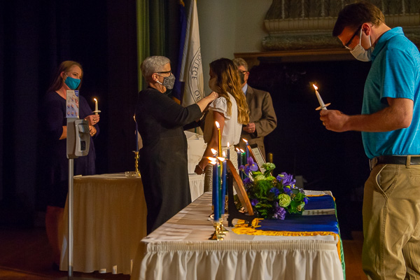 President Davie Jane Gilmour (whose personal hand-sanitzer dispenser allowed her to acknowledge each of the students as they crossed the stage) pins Courtney M. Case while Jack C. Dincher affirms his membership. Keeping the procession running smoothly were co-advisers Tammy A. Miller (left), who held the inductees' candles while they greeted the president, and Marc E. Bridgens, behind the bound Alpha Chi constitution signed by each new member.