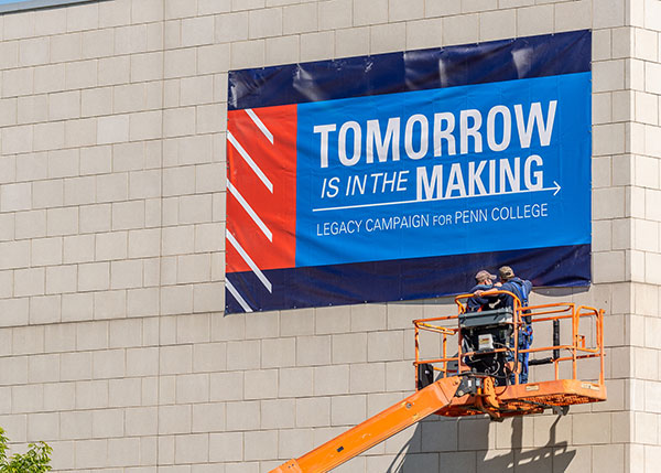 A banner announcing the Legacy Campaign for Penn College is installed Thursday morning on the Student & Administrative Services Center.