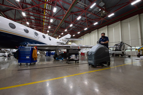 Second-shift custodian Edward A. Crawford operates a large floor-scrubber in the spacious Aviation Center hangar.