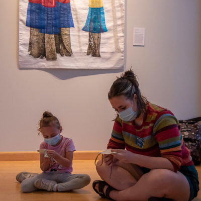Chloe N. Taylor (right), gallery attendant and graphic design student, works with a youngster on hand-sewing fabric blocks.