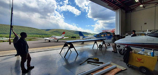 The hangar's scenic southern exposure sheds light on Matthew Spory, Roger Bohner and his son, Grace Snyder and Robby Ford as the group prepares to reattach the wings onto the fuselage.