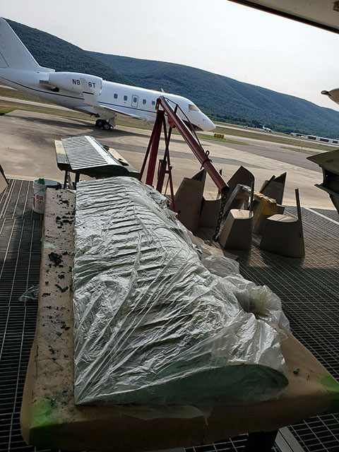 To ensure adequate preparation before applying paint, the surfaces of the entire aircraft had to be stripped down to base metal or fiberglass. Here, the flaps are covered in paint stripper and wrapped in plastic to keep the area moist enough for the chemicals to work properly. The paint would be wiped off after anywhere from 30 minutes to a few hours, leaving a clean metal surface. On parts that are made out of composite material, the paint needed to be sanded off by hand.