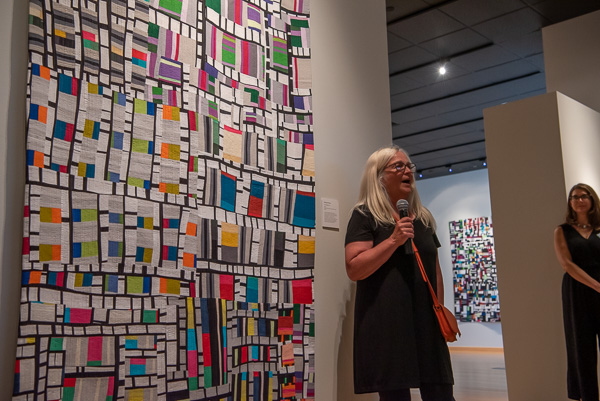 Margaret Black’s two abstract quilts (in the foreground and background) bring dynamic dashes of color to the space. (Gallery Director Penny Griffin Lutz listens at right.)