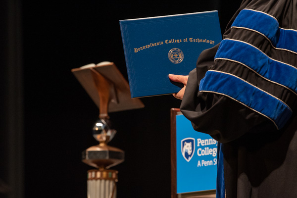 President Gilmour prepares for one of 150 handshakes on the day alongside another commencement tradition: the college mace, designed by her alumnus/retiree husband, Fred.