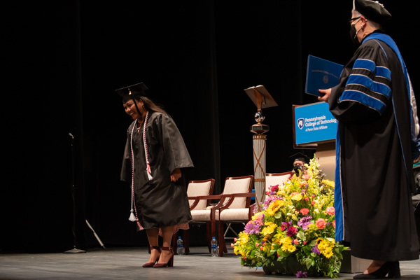 The student speaker, the last of the day's graduates to cross the stage, pauses in mid-stroll to acknowledge the audience's warmth.