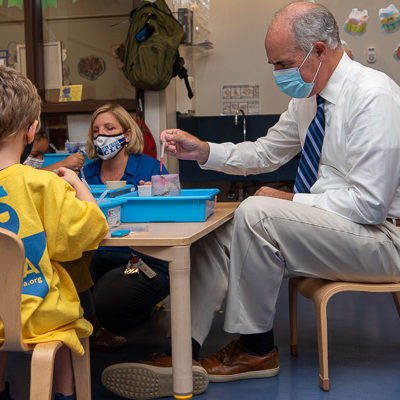 Getting down to the children's level, Casey takes a tiny seat for a hands-on science experiment with group leader Neva E. Simcox (center) ...