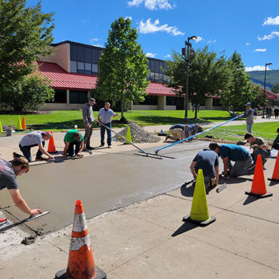 Reber (standing, in blue shirt) works with his Concrete Construction class on Wednesday, restoring sidewalks near the Larry A. Ward Machining Technologies Center and the Lycoming Engines Metal Trades Center.