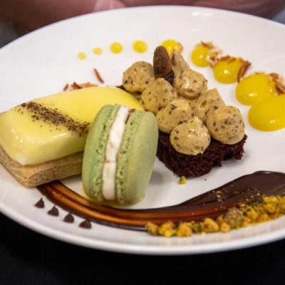 The featured dessert from Mitchell’s Art of Food: a trio of lemon Bavarian with mirror glaze on a black pepper cookie; coconut key lime French macaron; and chocolate chiffon cake with pistachio buttercream.