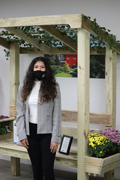 Lizeth V. Reyes-Becerra, of Erie, a building construction technology student and member of the Penn College Construction Association, stands in front of an outdoor bench created by the organization for the silent auction.