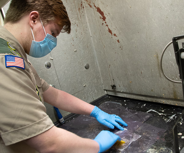 A Scout smooths resin over glass fiber to create a composite sheet in the plastics program’s Materials Testing Lab.