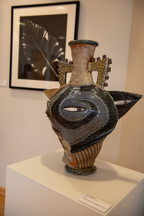 A large vessel form (coil constructed and soda fired stoneware) crafted by Stabley, with one of Vanderlin’s photo prints in the background