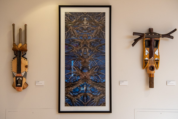 Vanderlin’s “Guardian Figure #3” print (center) is bookended by Stabley’s carved pine masks with mixed-media additions.