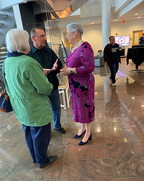 Brenda and Marlin Cromley, members of the Ambassador's Society who endowed a veterans' scholarship, talk with Gilmour near the Donor Wall.